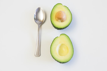 Two halves of avocado with core and spoon. Top view. Isolated objects on white background. Fresh food or healthy diet concept