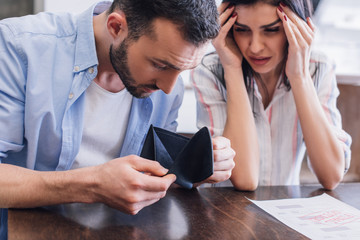 Man looking at empty purse near stressed woman at table with document