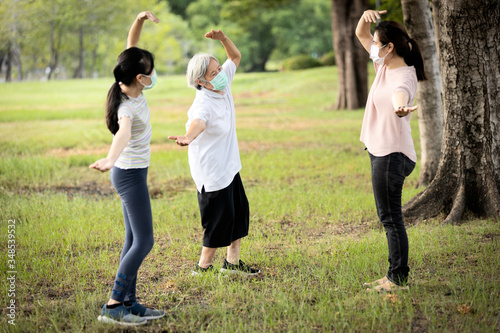 Asian woman is doing exercise activity for the old elderly and child girl,family workout,wearing protective mask outdoor at park,work out outside home after Coronavirus quarantine or Covid-19 lockdown