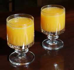 Food still life: two crystal glasses with fresh pressed orange juice on a wooden table