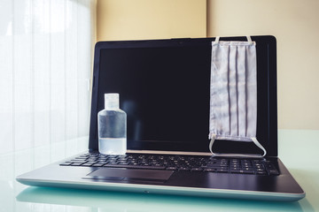 Photo of a laptop with cleaning and health objects such as face mask or disinfectant. Symbolizing new way of working at home.