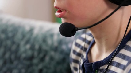 Wall Mural - leisure, children, technology and people concept - boy in headphones with microphone and gamepad playing video game at home