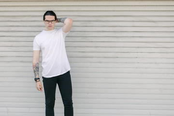 Wall Mural - Hipster handsome male model wearing white blank t-shirt with space for your logo or design in casual urban style. He is holding a skateboard
