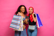 © Confidence - beautiful young back women carrying shopping bags viewing content on a mobile phone together, feeling excited
