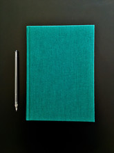 Top View Of Closed Green Cover Notebook With Pencil On Black Desk Background