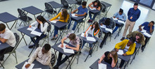 Instructor Supervising High School Students Taking Exam At Desks