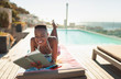© Paul Bradbury/Caia Image - Smiling, carefree young woman reading book at sunny poolside