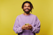 © timtimphoto - Happy young handsome brown haired man with dreadlocks smiling cheerfully at camera while holding mobile phone, dressed in purple sweatshirt while being isolated over yellow background