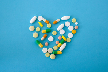 colorful pills and capsules in the shape of a heart on a blue-green background located in the center of the image, love, isolated