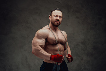 Shirtless adult male bodybuilder doing a biceps showing with a smile in a bright studio