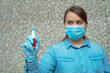 young woman in a blue protective mask holding a red spray sanitizer for hands.