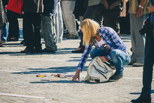 Young Woman Dropped A White Purse And All Contents Have Dropped On The Floor. Woman Picking Up Contents Of Purse Or A Bag In A Crowd.