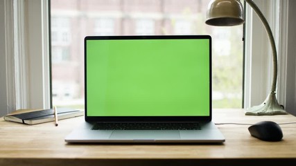 green screen laptop computer sitting on a home work desk next to a desk lamp. footage shot with red,