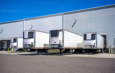 Refrigerator semi trailers without semi trucks standing at warehouse dock gates loading frozen cargo for next freight