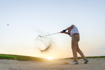 Golfers exploding sand in the bunker.