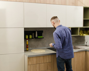 Wall Mural - A bearded man stands with his back to the camera next to a work surface in a modern kitchen