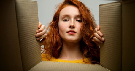 Wall Mural - Young cheerful girl getting parcel at home. Pretty girl sitting on sofa at home and opening carton box. Mail delivery to house.