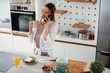 © JustLife - Young woman in kitchen. Beautiful woman drinking coffee and talking to the phone.
