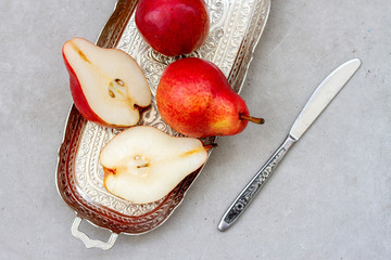 Ripe pear on silver tray with a knife. Pieces of fresh pear on gray background