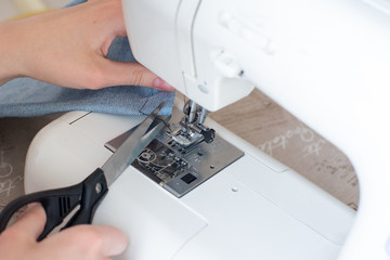 Close-up of sewing on a sewing machine, a hand with scissors cuts the thread. The concept of a hobby, design, self-creation of exclusive things