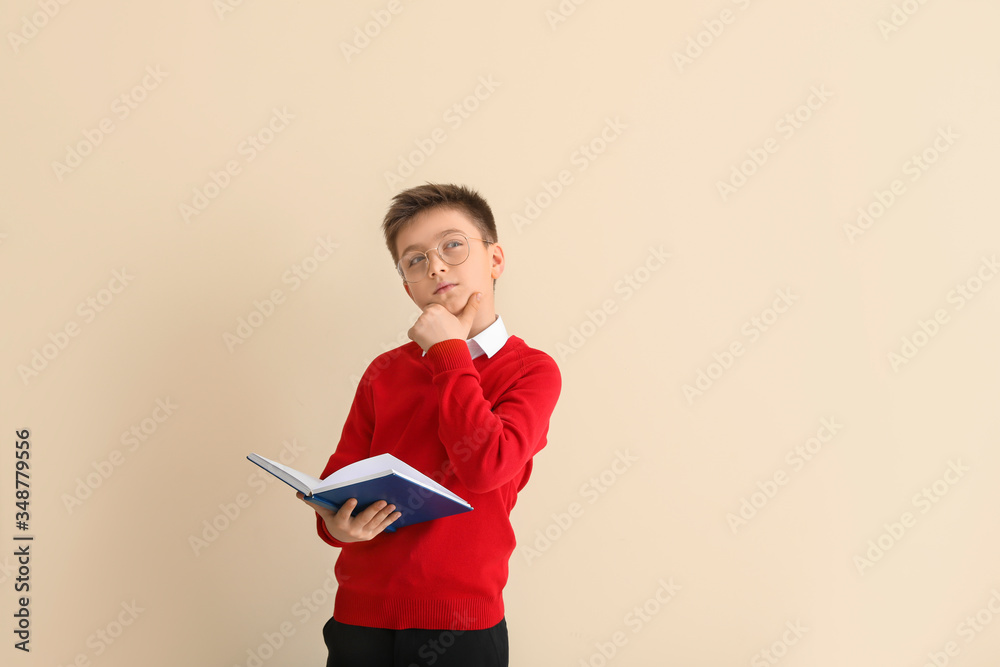 Thoughtful little pupil with book on color background