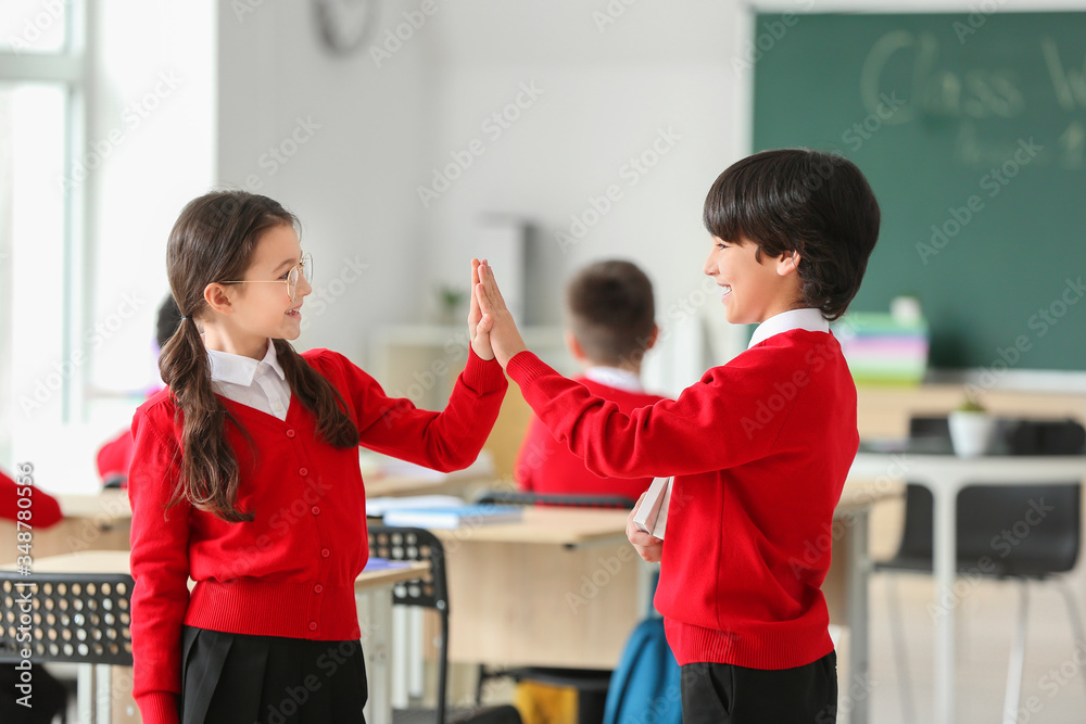Cute little pupils giving each other high-five in classroom