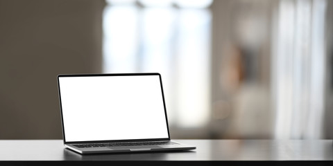 Wall Mural - Photo of white blank screen computer laptop putting on working desk over comfortable living room as background.