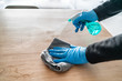 Surface cleaning spraying antibacterial sanitizing liquid with bottle washing table top at home . Man using gloves and towel doing spring cleaning.