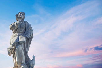 Wall Mural - Ancient stone statue of St. John the Evangelist with eagle against blue sky.