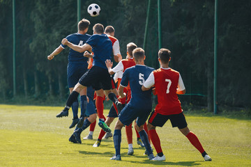 Soccer players heading the ball in competition. Football adult game. Players in two teams compete for the ball. Footballers jumping high on the grass pitch