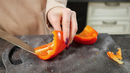 Wall Mural - accurate woman with nice manicure cuts fresh red Bell pepper using big knife preparing salad for family closeup