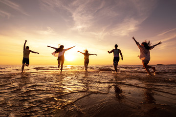 five happy friends runs at sunset beach