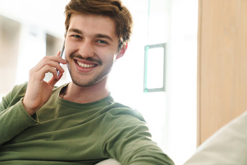 Photo of cheerful young man smiling and talking on smartphone