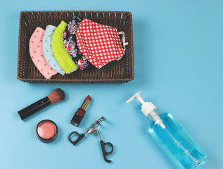 fabric face masks in rectangle basket with alcohol hand gel and woman's make up accessories on blue background..protection from coronavirus of covid-19,new normal life style concept.