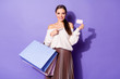 © deagreez - Positive cheerful girl shopping center client point index finger white paper card indicate she can pay packages wear off-shoulder white jumper sweater skirt isolated violet color background