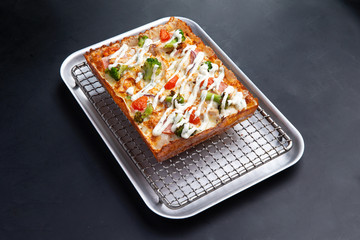 detroit pizza on an iron tray on a dark background. selective focus