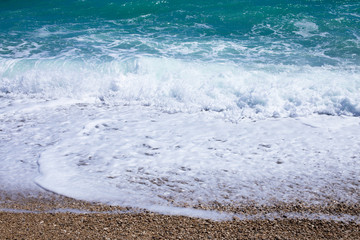 Wall Mural - Sea waves background with small pebbles and foam of ocean water, place for text.