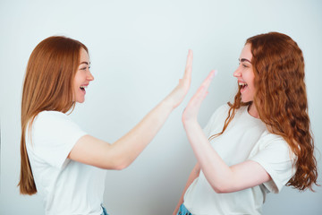 two redheaded young women both wearing t-shirts standing on isolated white backgroung look positive giving each other high five, body language concept