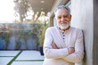 Portrait Of Smiling Retired Senior Hispanic Man In Garden At Home Against Flaring Sun