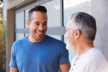 Wall Mural - Senior Hispanic Man Talking And Laughing With Adult Son In Garden At Home