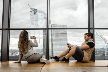 Wall Mural - Beautiful young woman taking photo of skyscrapers, while her man is playing with his phone, London, UK.