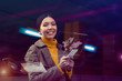Embracing a technological future concept. A beautiful young Asian woman is being surrounded by a cyberpunk environment where all technology apps are projected as holograms from her phone around her. 