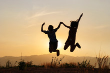 Silhouette Of Happy Little Boy And Girl Jumping Playing On Mountain At Sunset Time