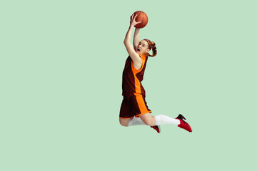 Young caucasian female basketball player in action, motion in high jump isolated on mint colored background. Concept of sport, movement, energy and dynamic, healthy lifestyle. Training, practicing.