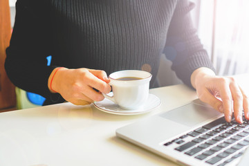 girl typing on a laptop keyboard, next is a mug of coffee