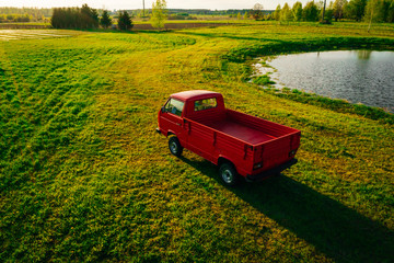 Aerial view on Classic red pickup truck on green farm land field in sunset time, Farmland transport