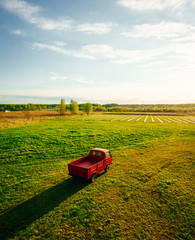 Aerial view on Classic red pickup truck on green farm land field in sunset time, Farmland transport