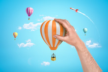 Hand Holding Orange White Hot Air Balloon With Silver Rocket And Hot Air Balloons On Blue Sky Background