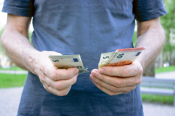 A man in a blue T-shirt counts small euro bills at 5 and 10. The concept of poverty and wealth