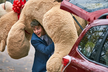 3/4 MCU Of A Young Man Grabbing A Large Teddy Bear From The Trunk Of His Car, Throwing It Over His Shoulder And Walking Off Camera.